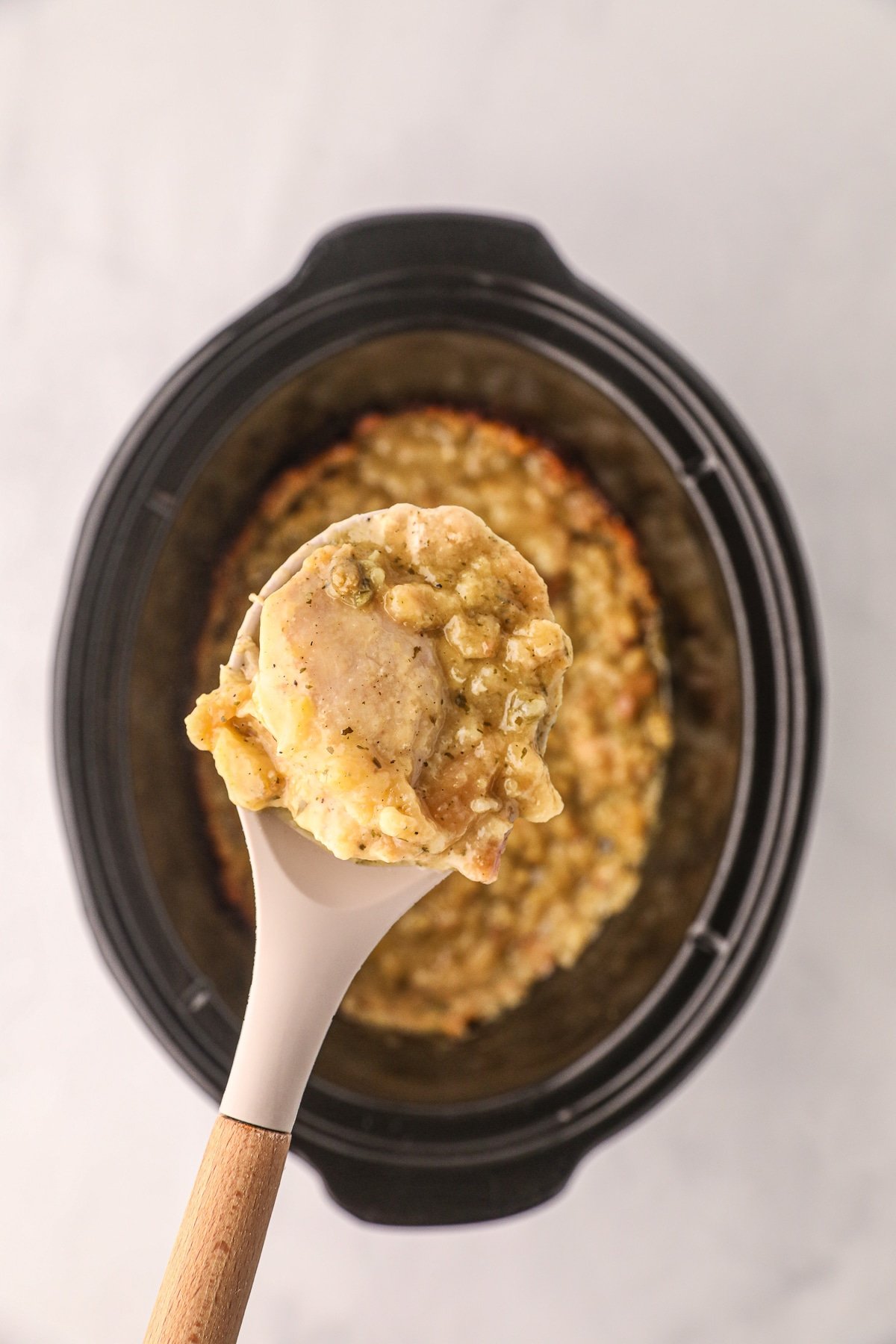 Chicken thigh and stuffing on a spoon coming from slow cooker.