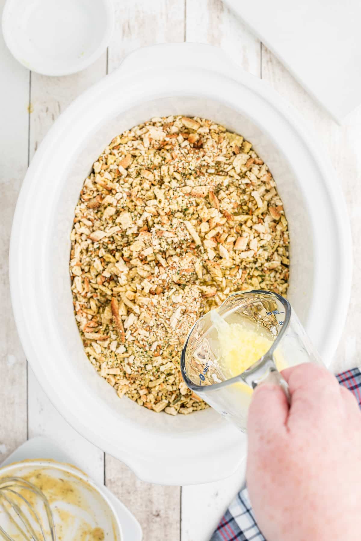 Stuffing on top of chicken in a slow cooker with butter being drizzled over.