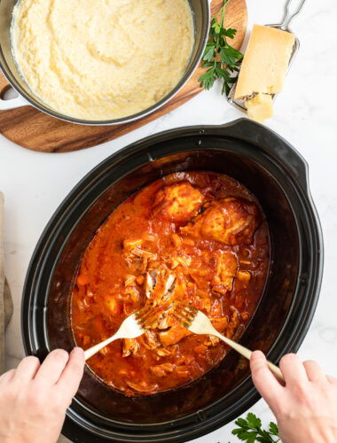 Chicken marinara being shredded with polenta on the side.