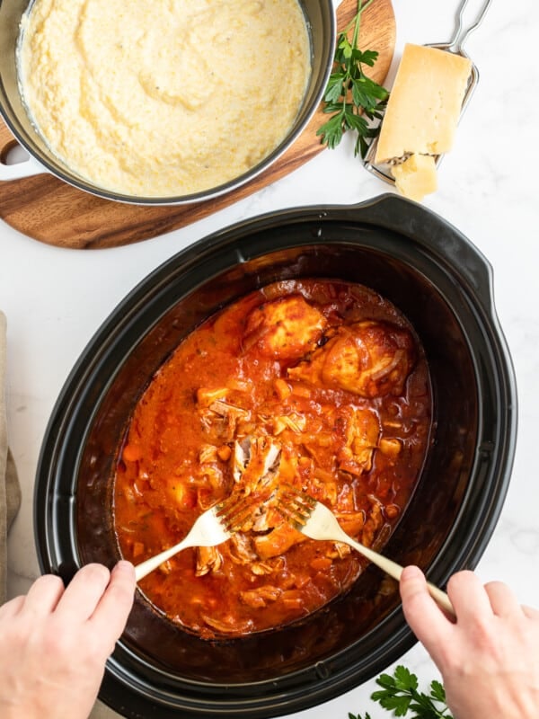 Chicken marinara being shredded with polenta on the side.