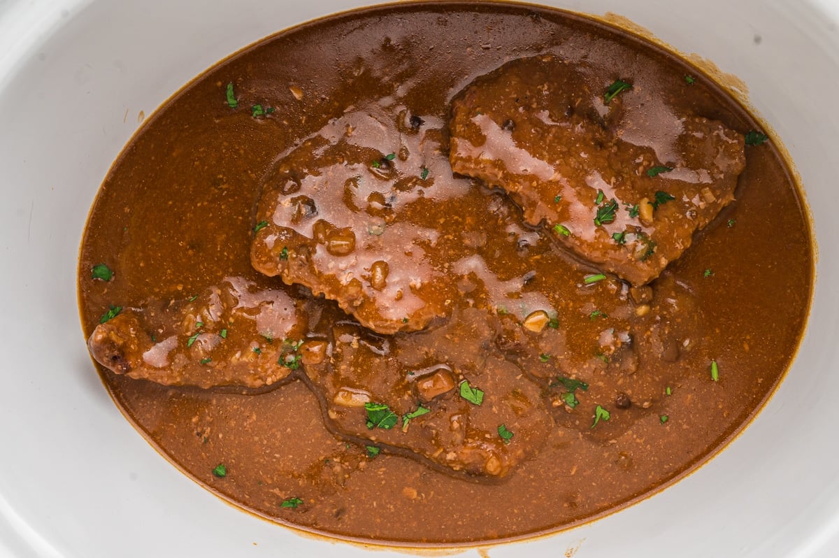 Cube steak in slow cooker with parsley on top.