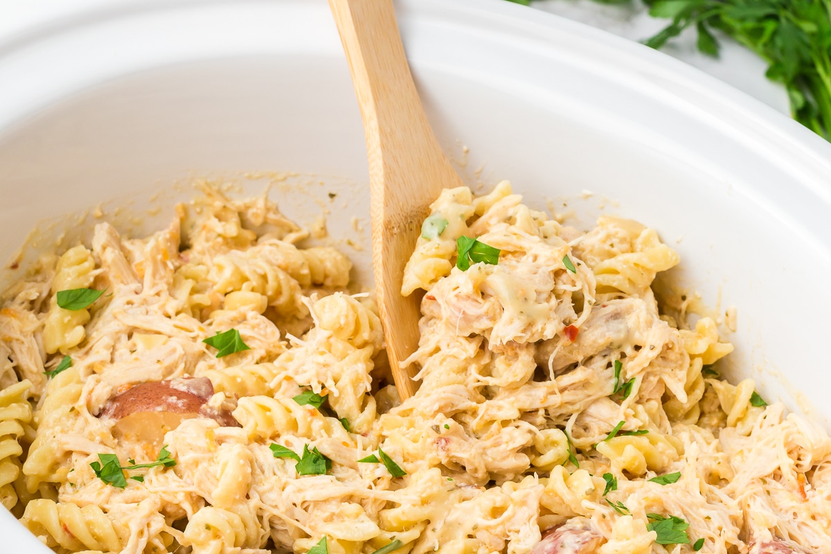 Spoon in rotini pasta with garlic in crockpot.