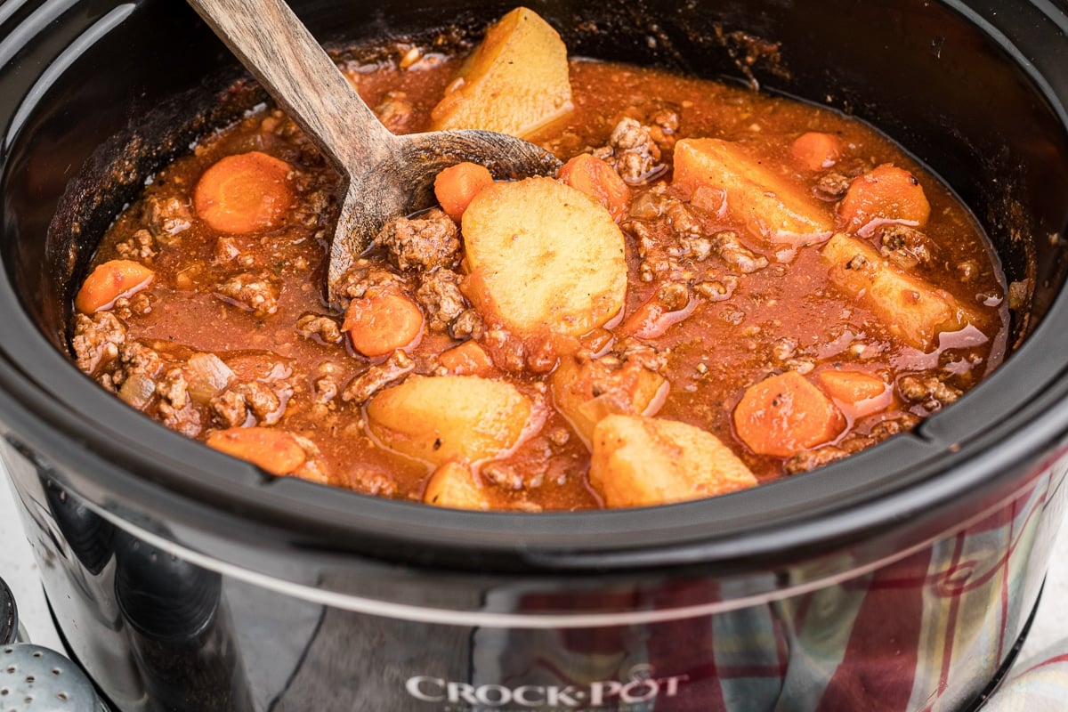 Side view of poor man's stew in crockpot with wooden spoon in it.