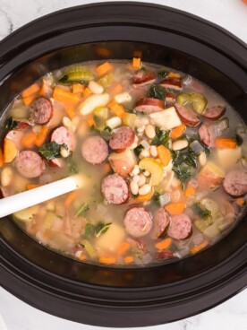 overhead shot of cooked sausage and bean soup in a slow cooker.
