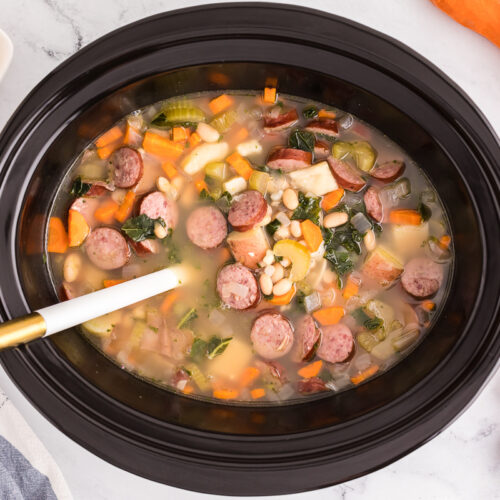 overhead shot of cooked sausage and bean soup in a slow cooker.