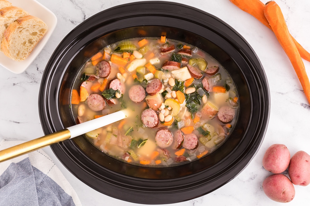 overhead shot of cooked sausage and bean soup in a slow cooker.