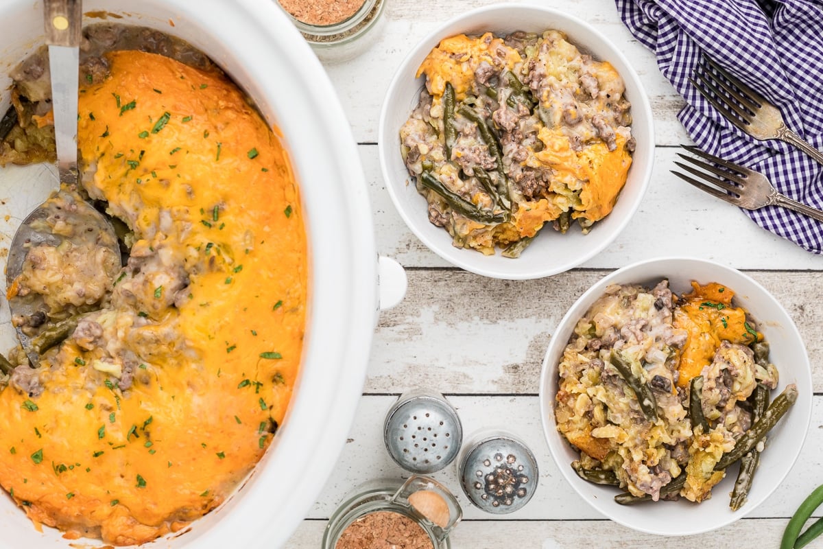 scoop of tater tot casserole out of crockpot and two bowl filled with it.