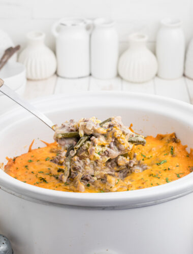 Scoop of tater tot casserole coming from crock pot.