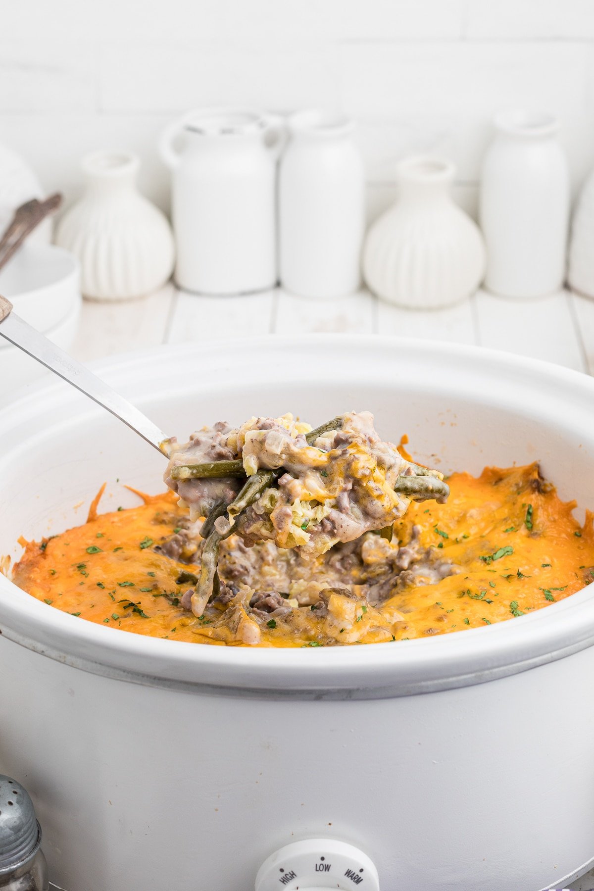 Scoop of tater tot casserole coming from crock pot.