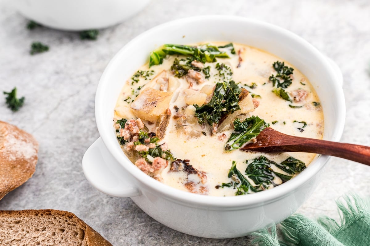Bowl of zuppa toscana with wooden spoon in it.
