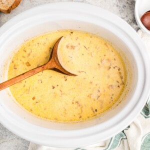 cooked beer cheese soup with a wooden spoon in it.