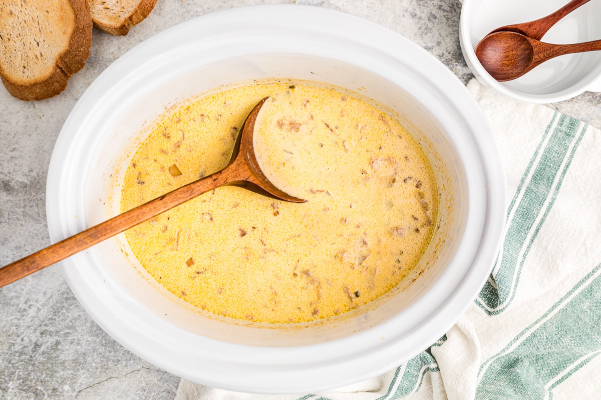 cooked beer cheese soup with a wooden spoon in it.