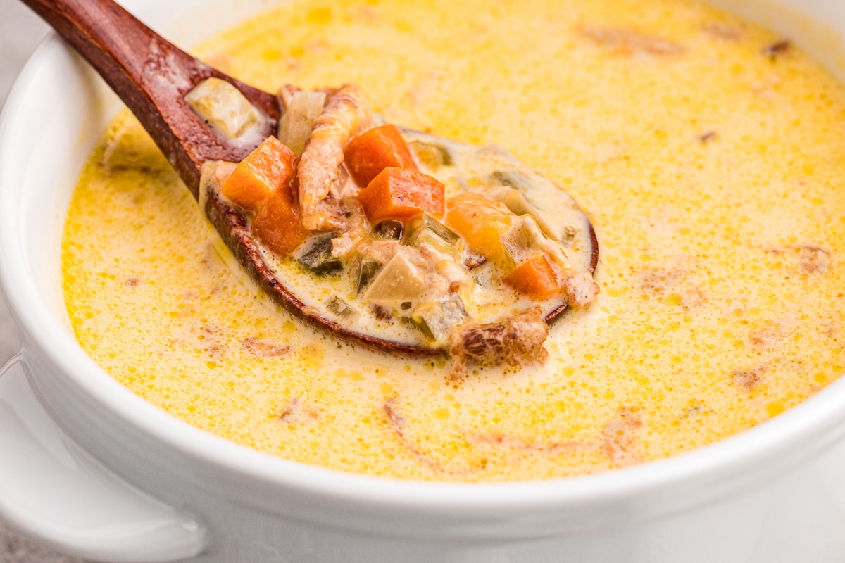 close up of beer cheese soup in a bowl with wooden small spoon.