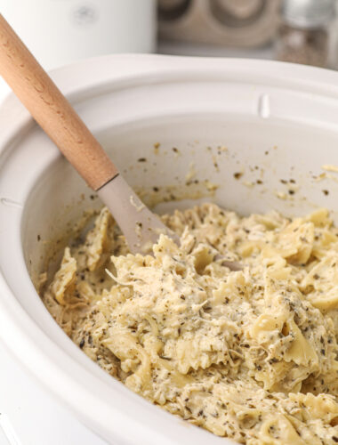 spoon in creamy pesto chicken pasta in crockpot.