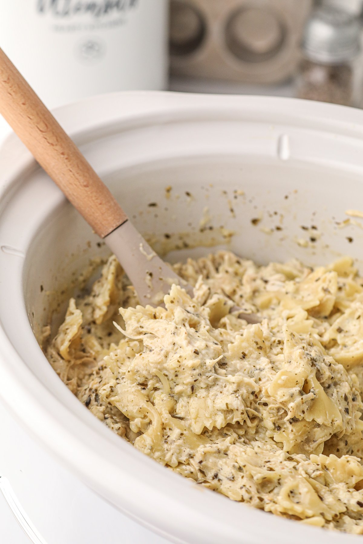 spoon in creamy pesto chicken pasta in crockpot.