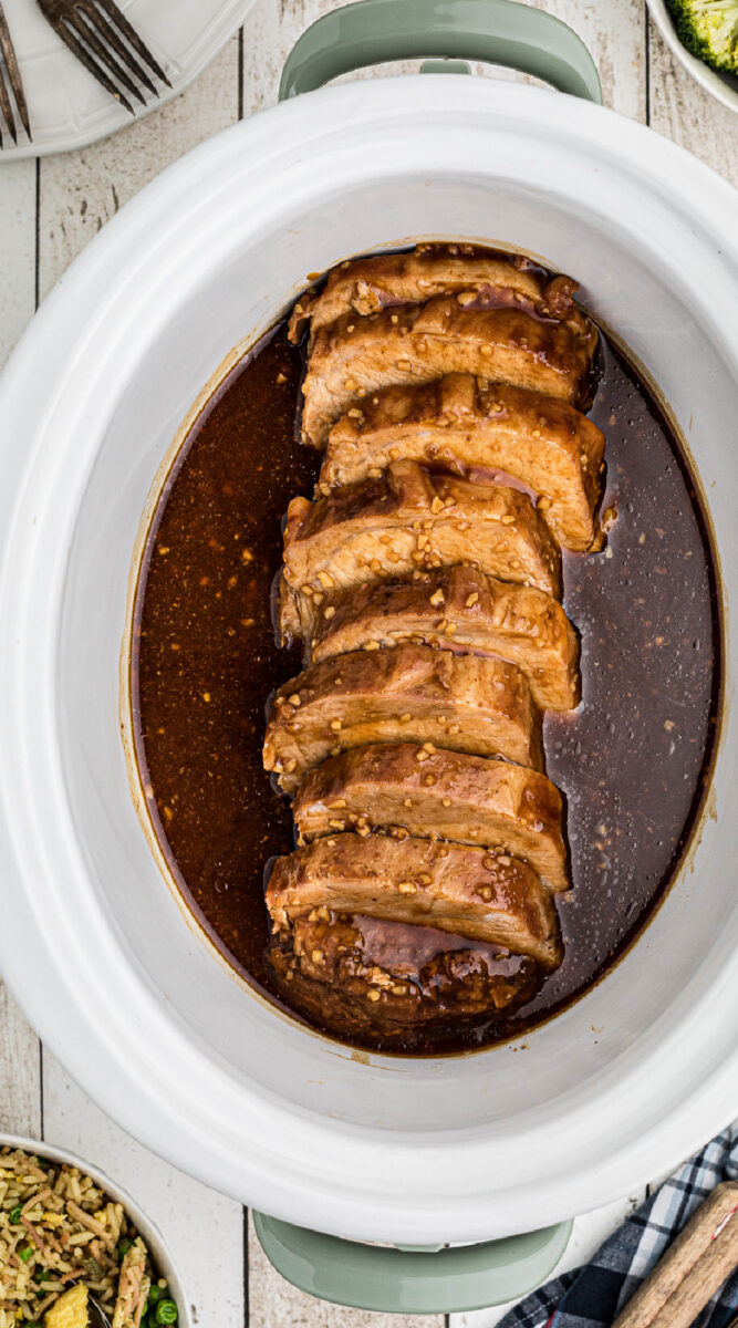 Long image of honey garlic pork loin slice in slow cooker.