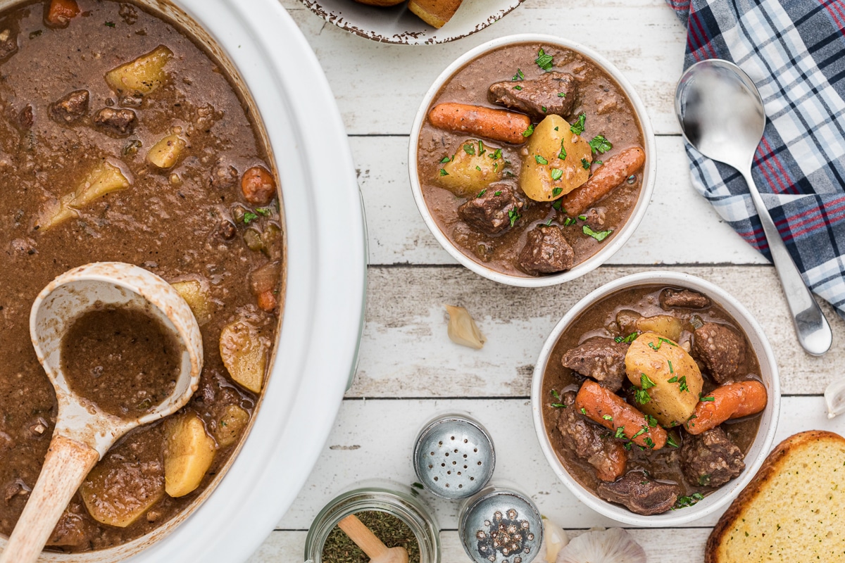Overhead image of venison stew in slow cooker and 2 bowls.