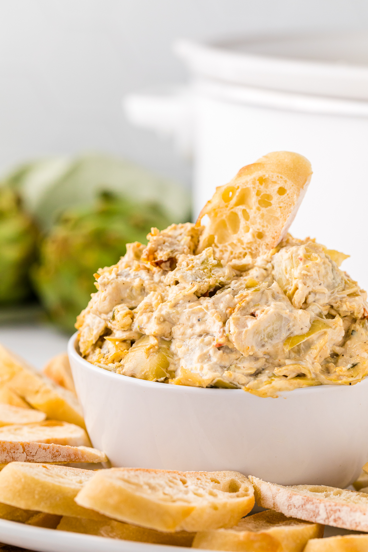 Artichoke dip in a bowl with a bread in it.