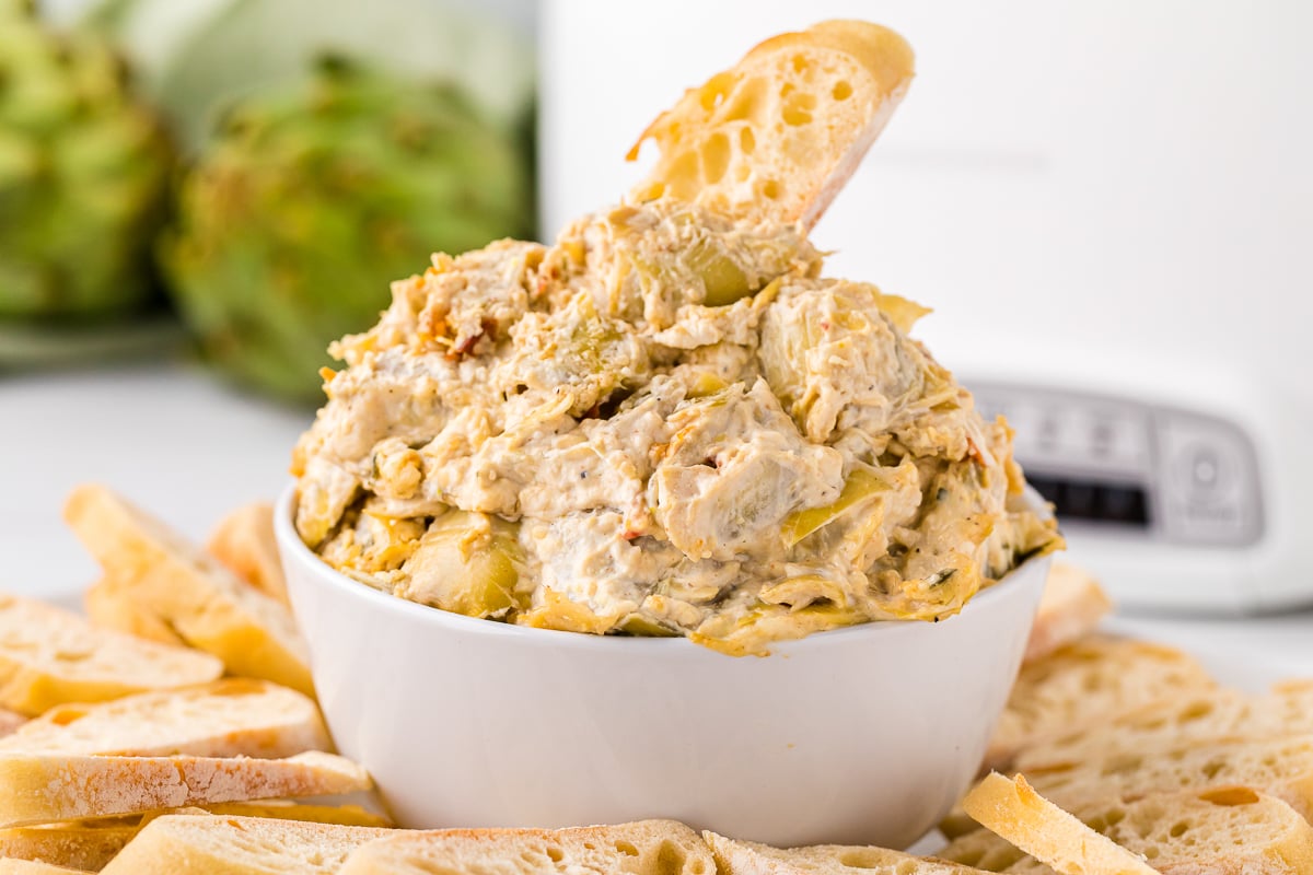 artichoke dip in a bowl with bread around it.