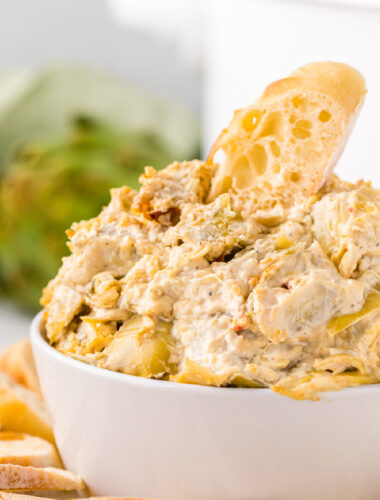 artichoke dip in a bowl in front of a crockpot.