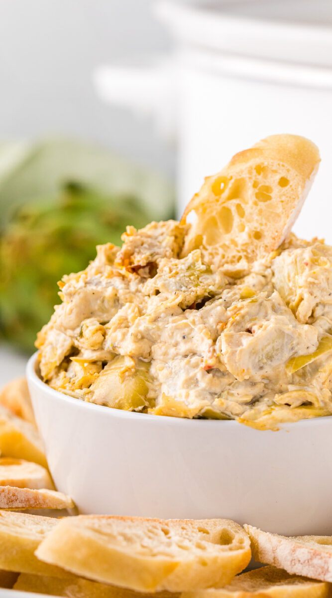 artichoke dip in a bowl in front of a crockpot.