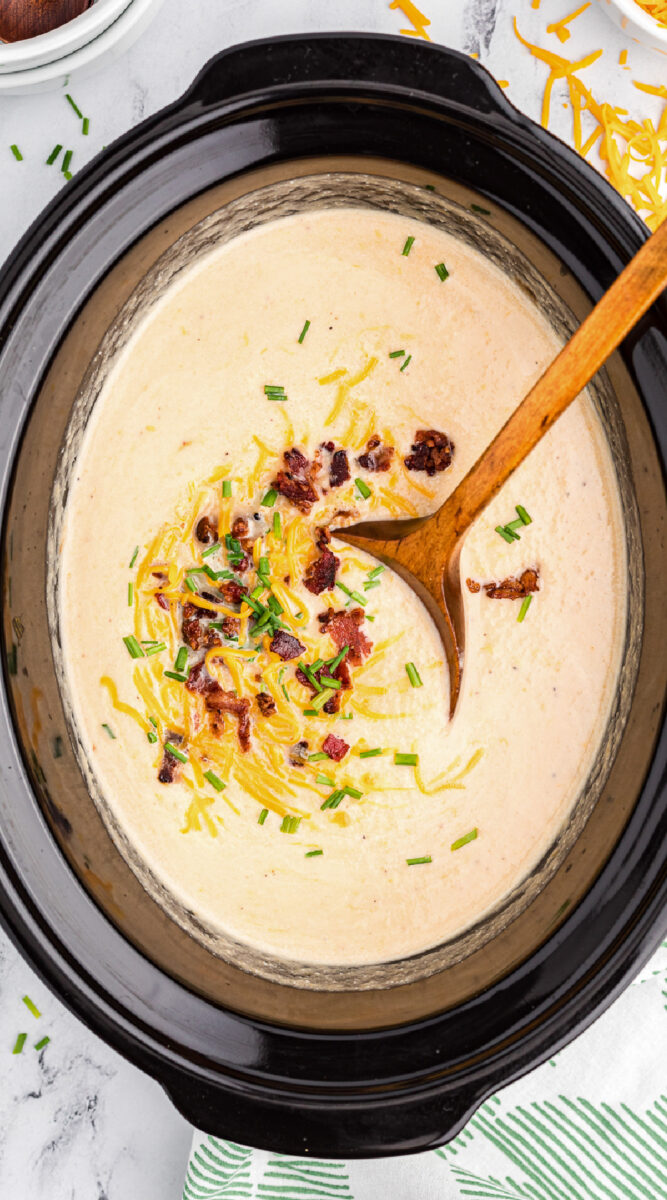 long image of cauliflower soup with bacon, cheese and chives on top.