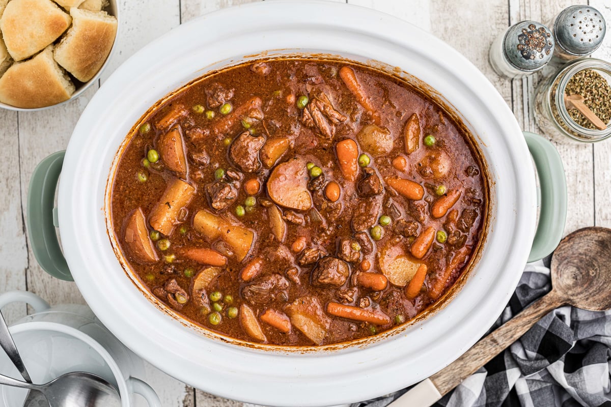 cooked beef stew in the slow cooker with rolls on the side.