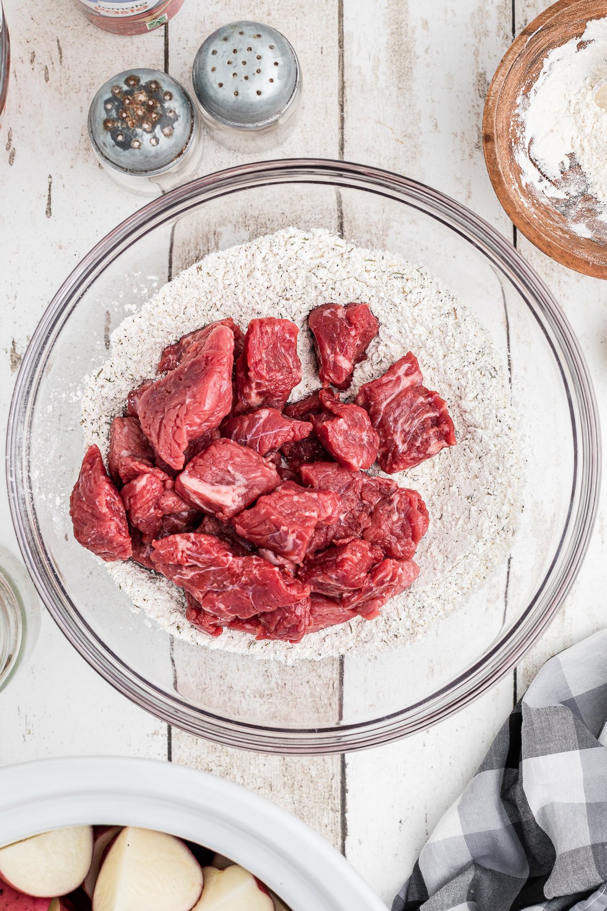 beef stew meat in a bowl of seasoned flour.