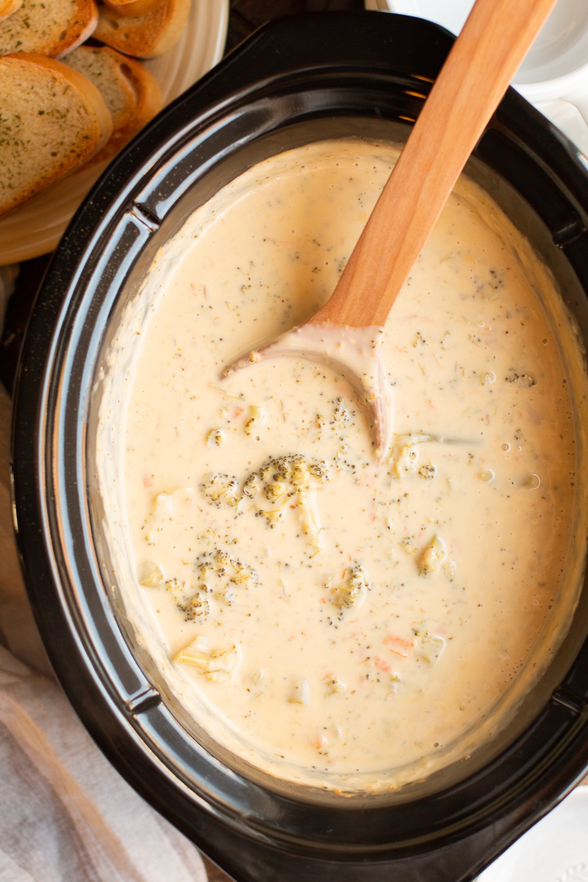 broccoli cheese soup in the slow cooker with a wooden spoon.