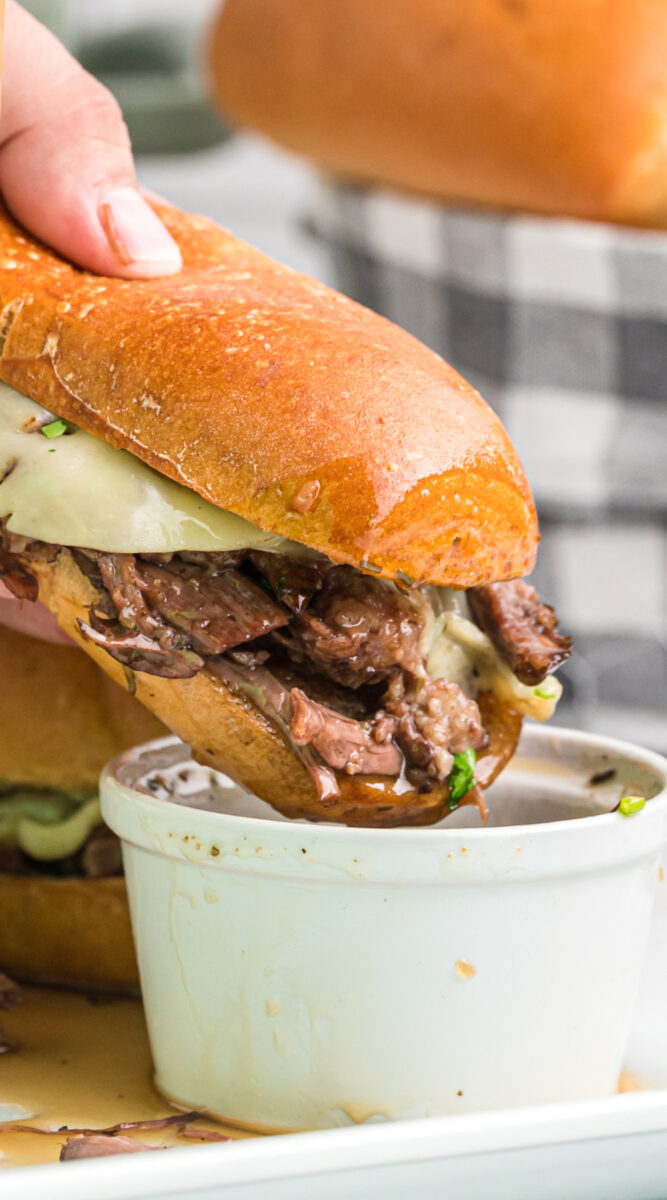 Long image of a french dip being dipped into au jus.