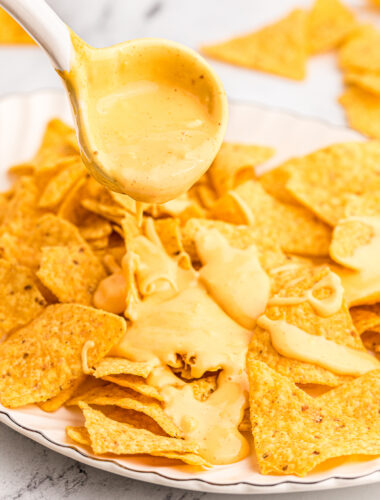 nacho cheese being pour over corn chips.