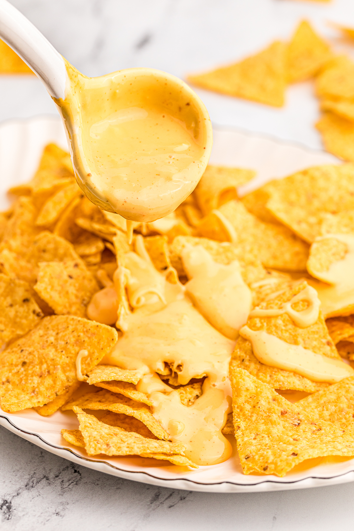 nacho cheese being pour over corn chips.