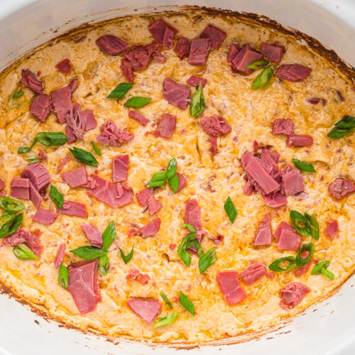 Cooked rueben dip with green onions and corned beef on top.