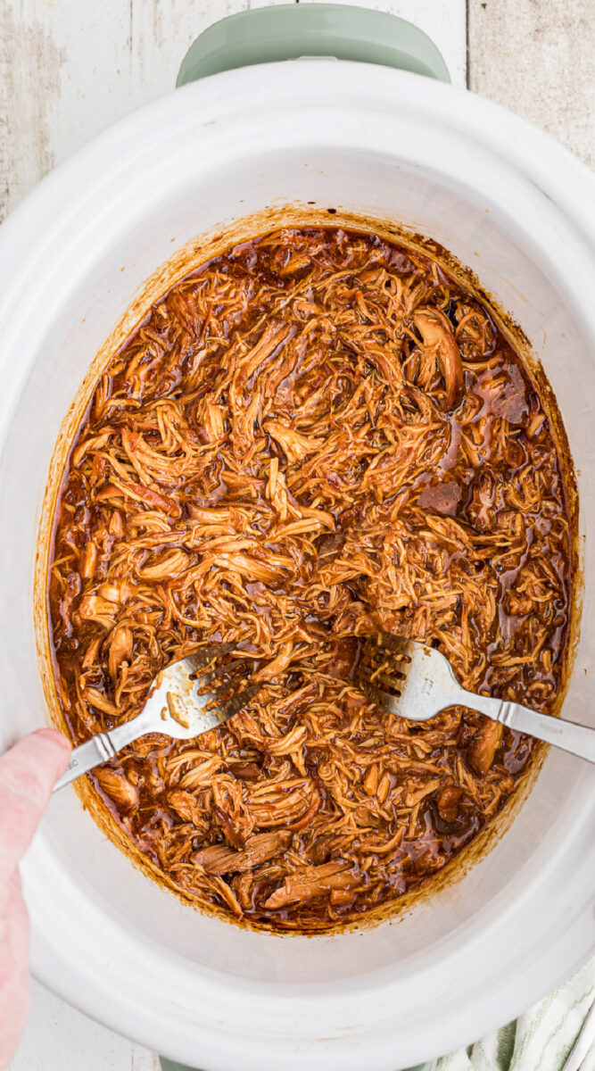 2 forks shredding chicken in a slow cooker.