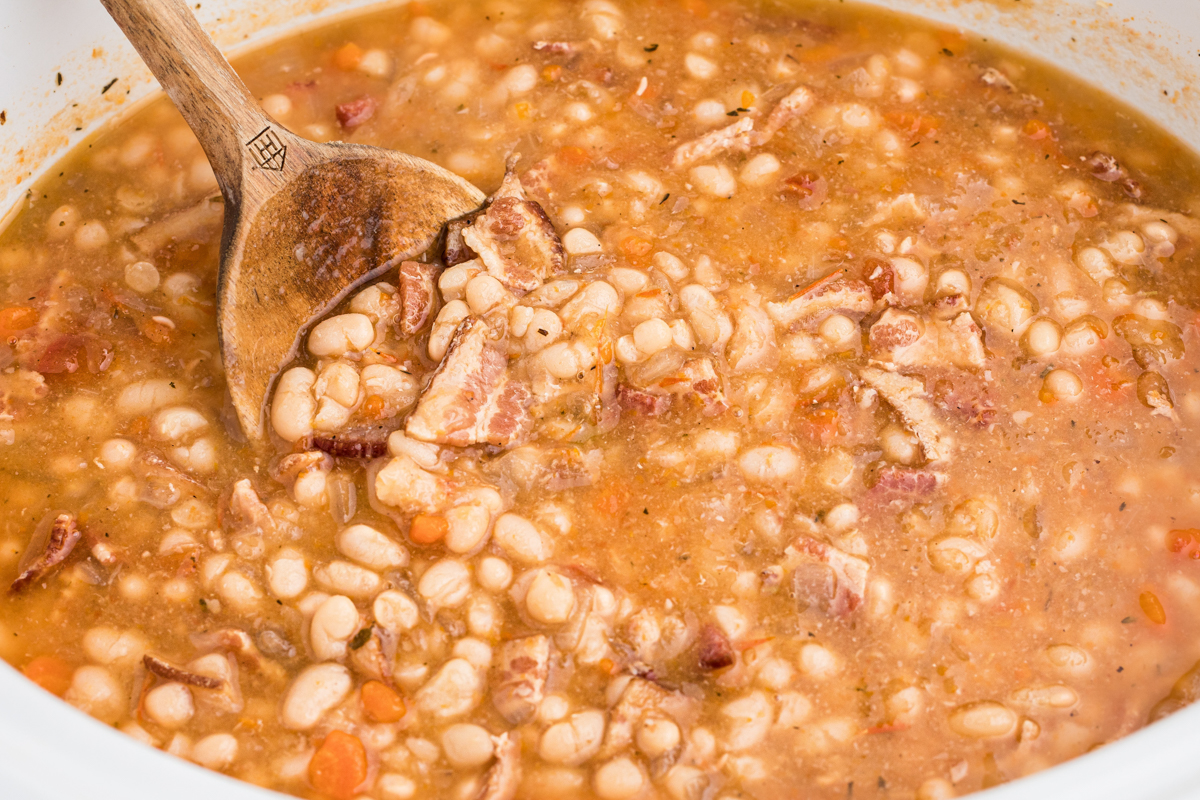 Bean and bacon soup (campell's copycat) in slow cooker with a wooden spoon.