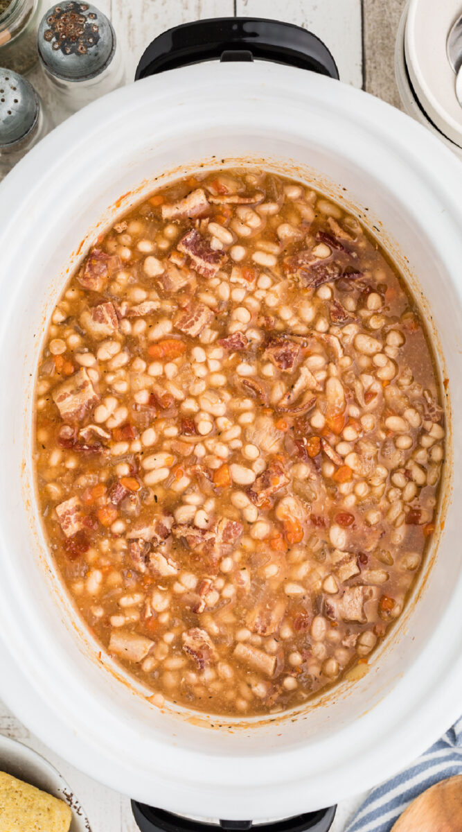 Long image of bean bacon soup in a white slow cooker.