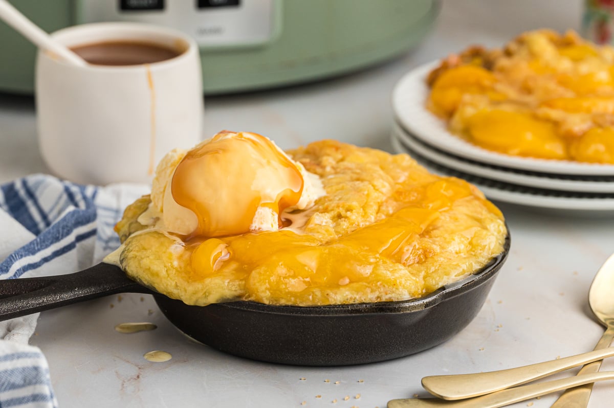 peach cobbler in small skillet with caramel on top of ice cream.