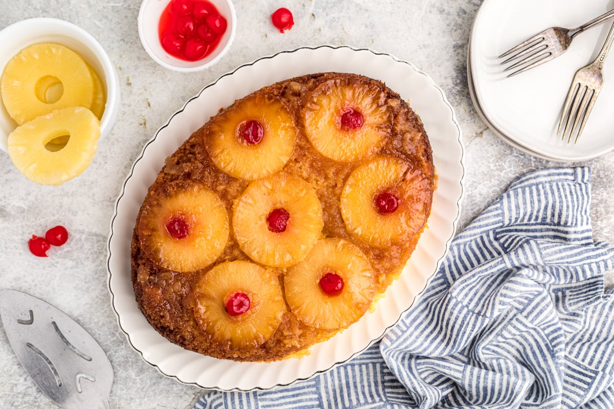 Pineapple upside down cake on a platter with plates next to it.