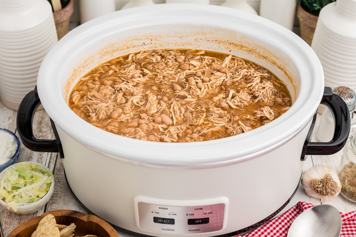 Beans and chicken in a white slow cooker with toppings on the side.