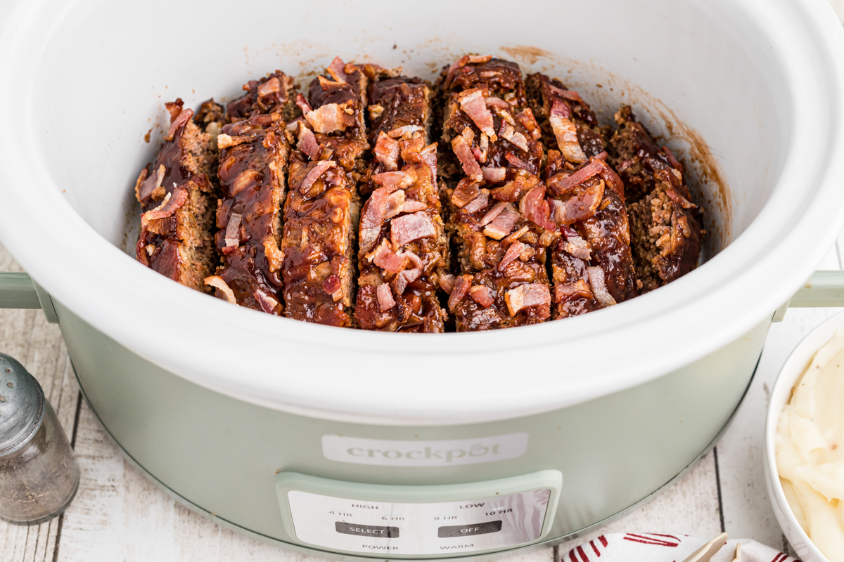 sliced meatloaf in a green slow cooker.