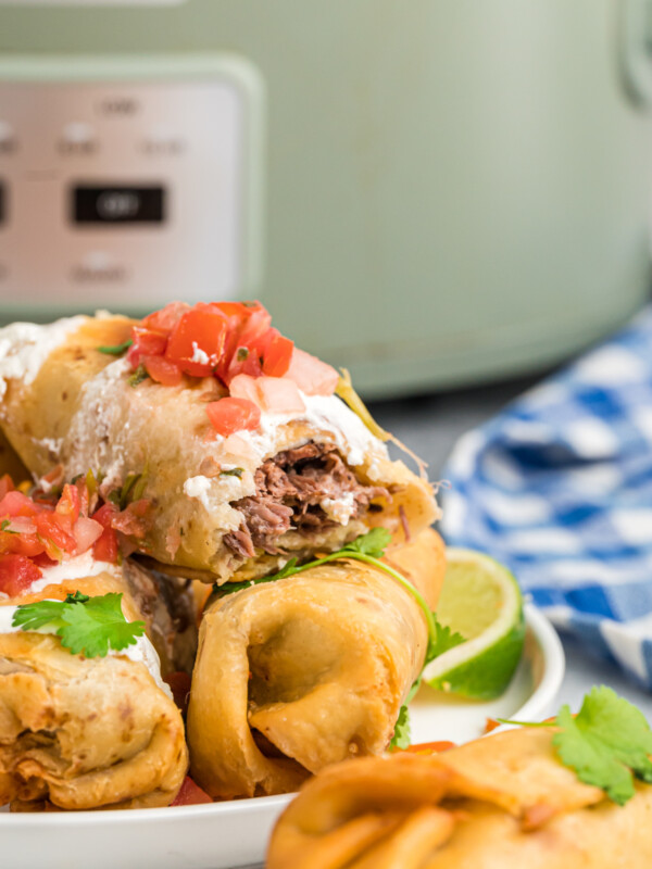 Stack of beef chimichangas in front of a slow cooker.