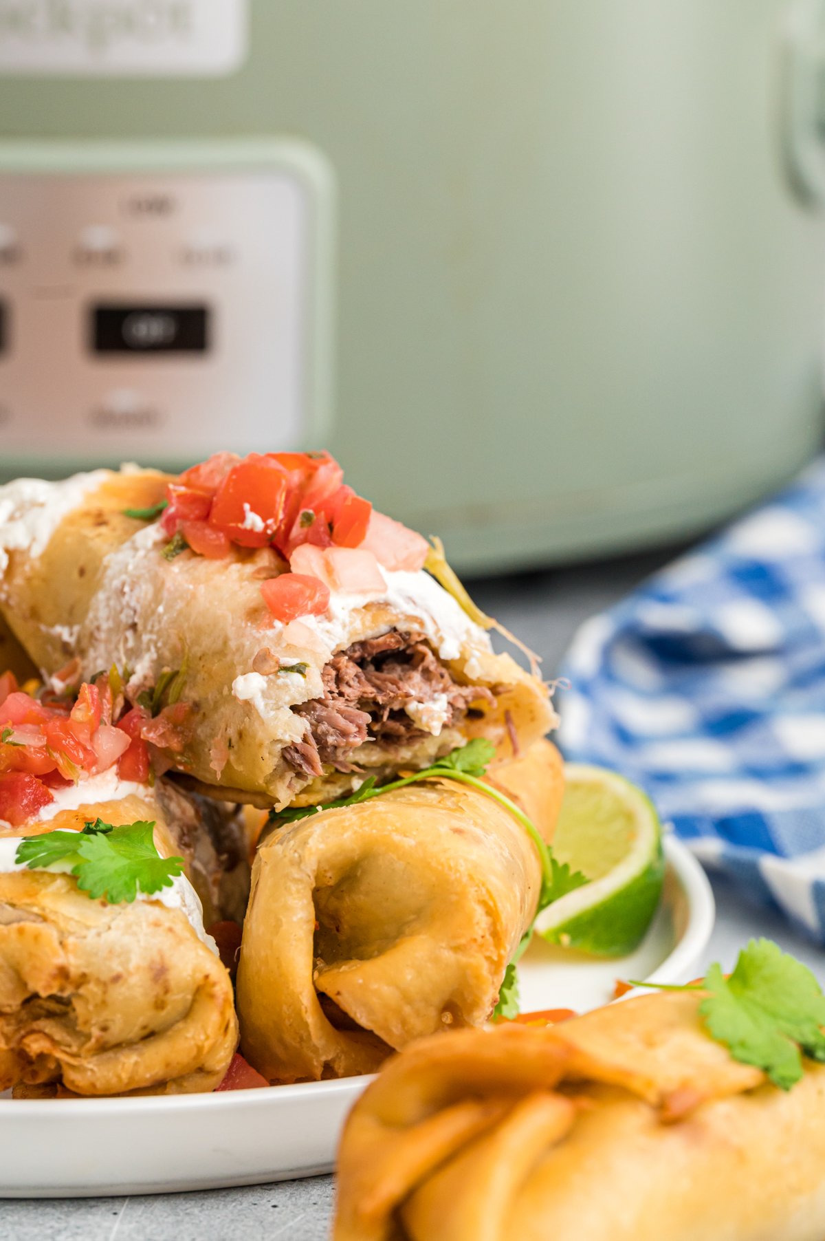 Stack of beef chimichangas in front of a slow cooker.