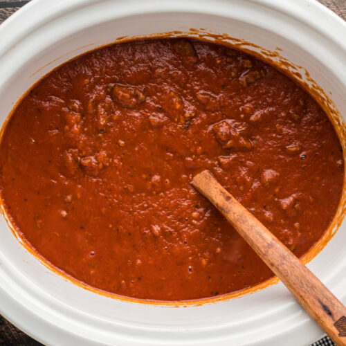 meaty bolognese sauce in slow cooker with wooden spoon.