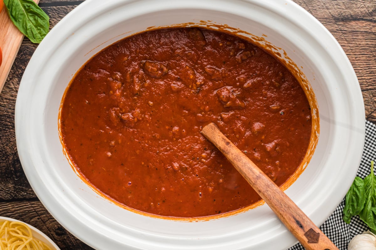 meaty bolognese sauce in slow cooker with wooden spoon.