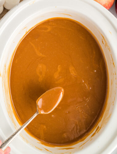 caramel dip on a spoon coming from slow cooker.