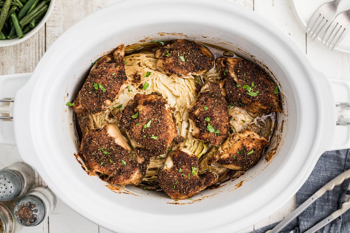 Overhead shot of chicken thighs and cabbage in a white slow cooker.