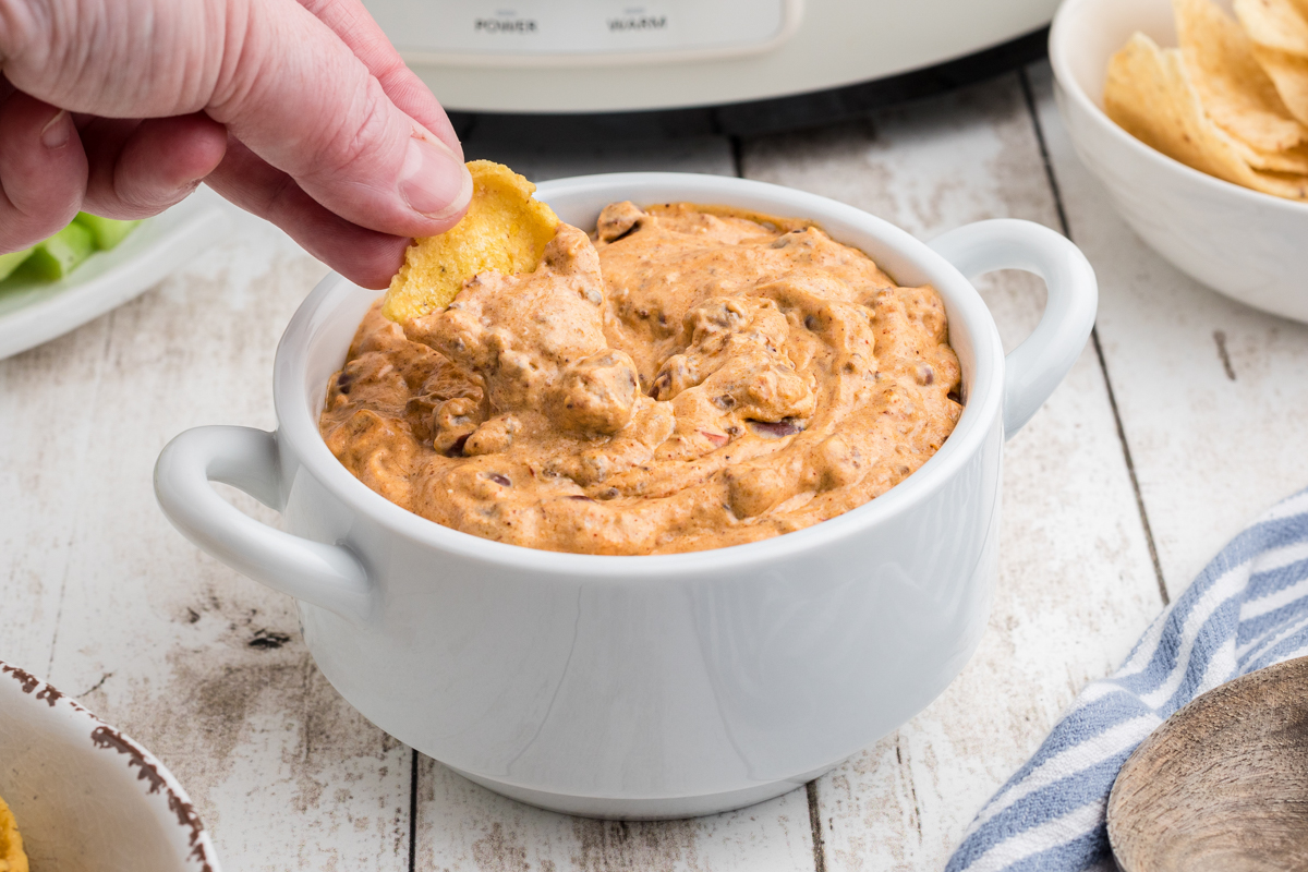 chili cream cheese dip in a bowl being dipped with a frito.