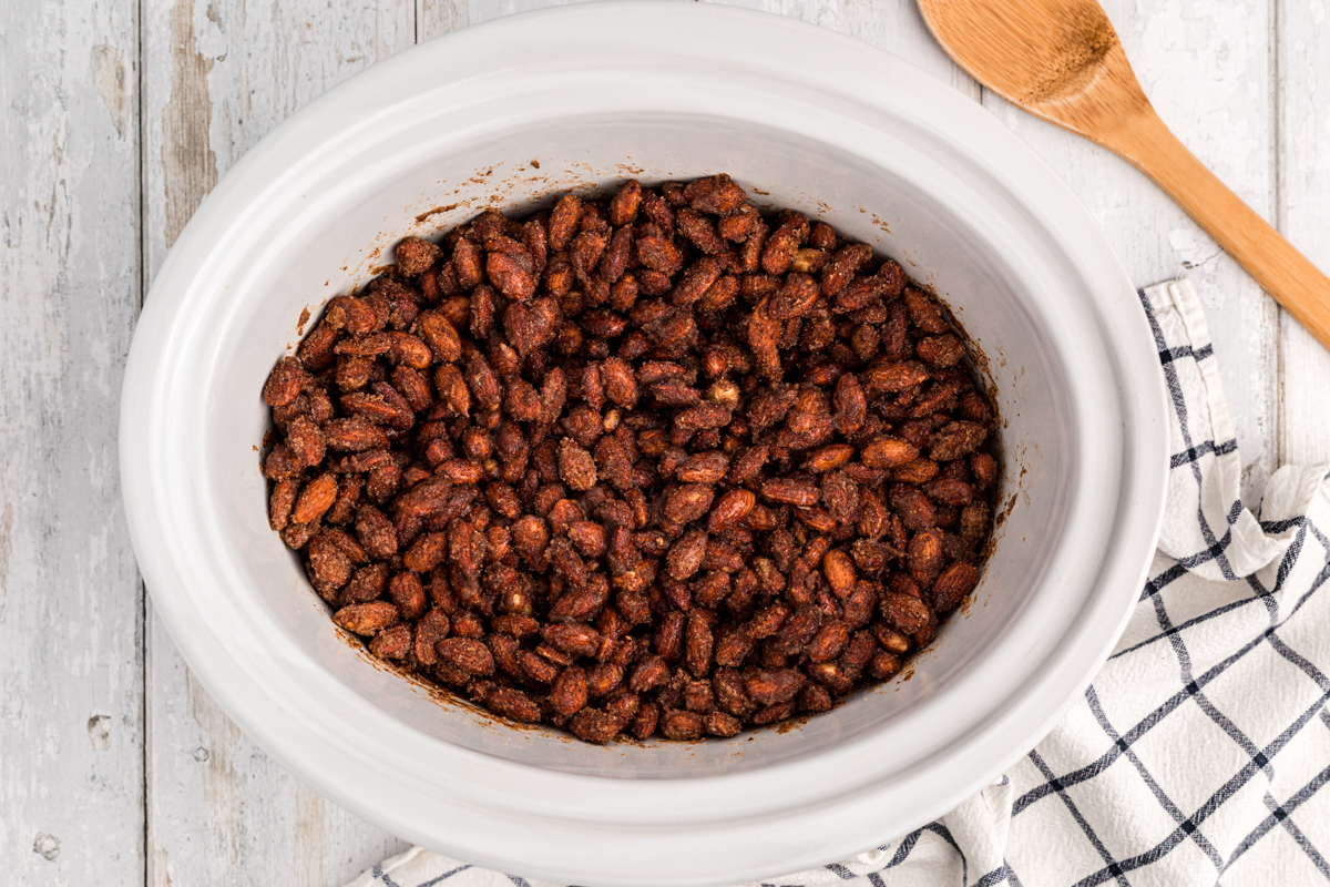 Overhead shot of cinnamon almonds in a white slow cooker.