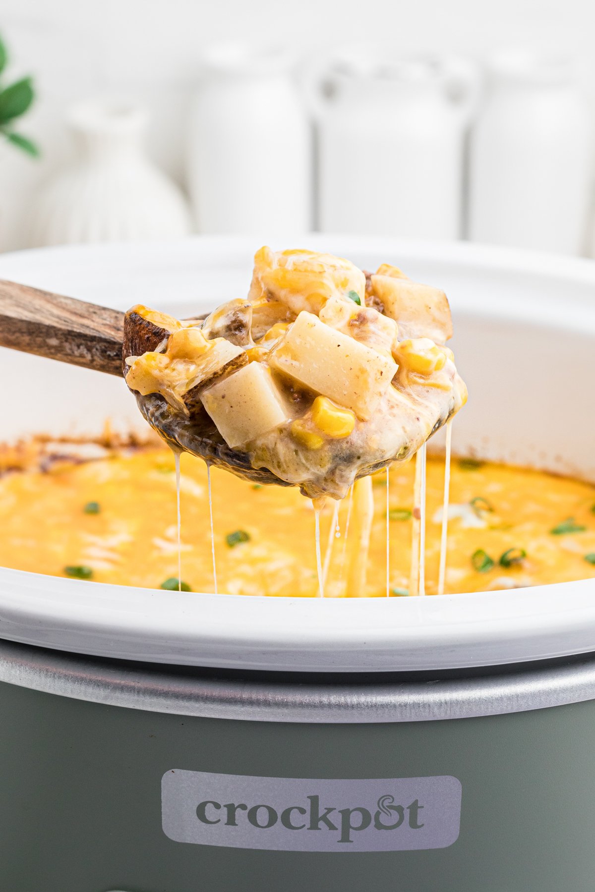 Scoop of hamburger hash on a wooden spoon coming from a slow cooker.