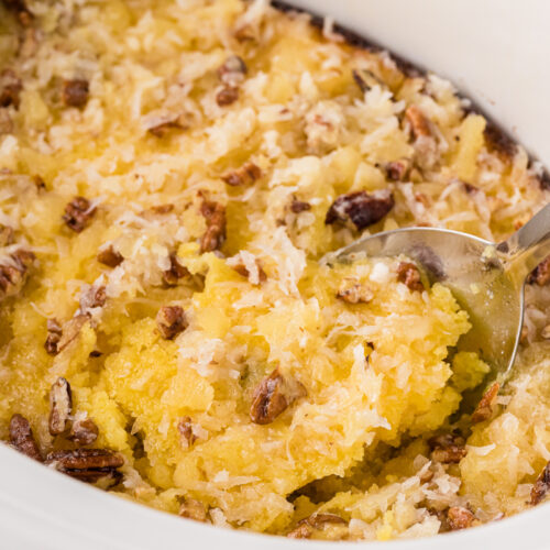 close up of pineapple spoon cake in a white slow cooker with a spoon.